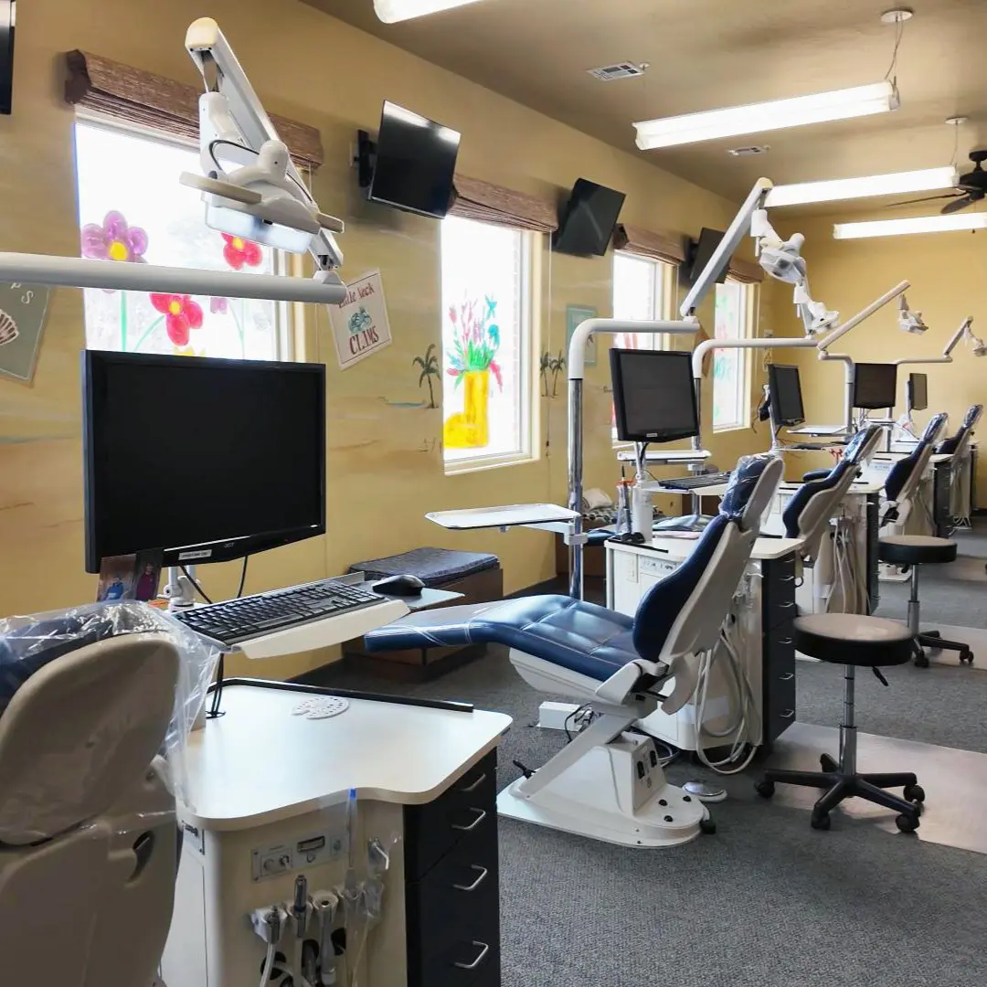 A bright, inviting dental clinic with multiple examination chairs lined up, each facing a screen. Colorful wall murals add a cheerful touch.