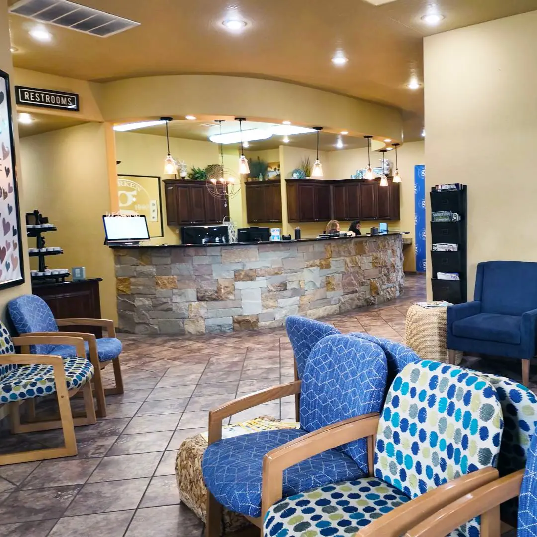 A cozy waiting area with patterned blue chairs and a stone-front desk. Warm lighting and decor create a welcoming atmosphere. A restroom sign is visible.